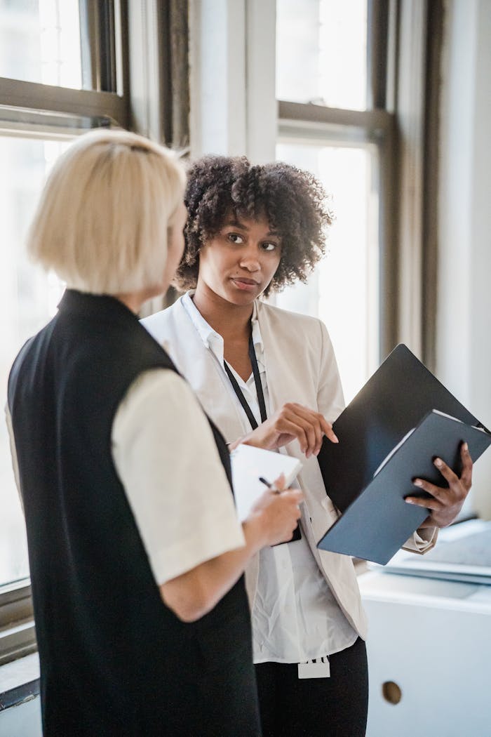 Two professional women discussing documents in a bright office setting.